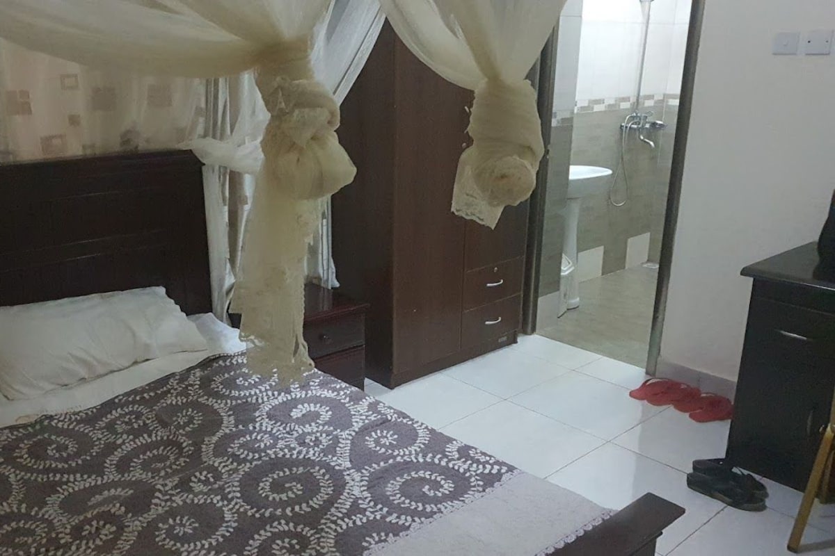 Une chambre d’hôtel comprenant un lit, une table de chevet, une armoire et une porte vitrée donnant sur une salle de bain.