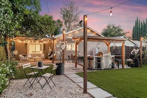 An outdoor patio area with a dining table, chairs, a hanging chair, and a grill station. - City of Trees House with Hot Tub & Game Room (West Sacramento)