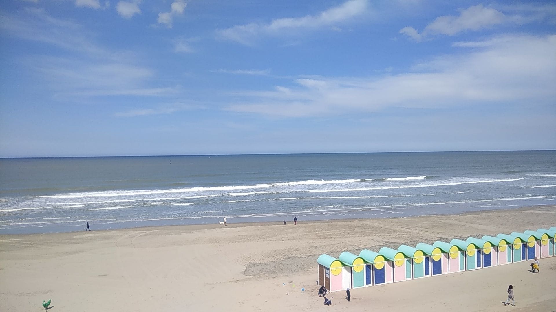 Een strand met een rij kleurrijke strandhuisjes en de oceaan op de achtergrond.