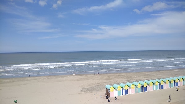Een strand met een rij kleurrijke strandhuisjes en de oceaan op de achtergrond.
