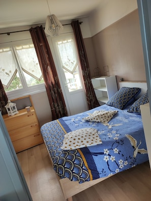Een slaapkamer met een bed, nachtkastje, dressoir en een raam met gordijnen.