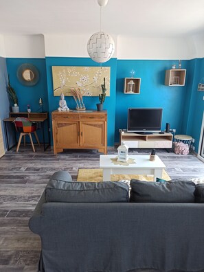 Ein Wohnzimmer mit blauer Wand, einer Holzkommode, einer Couch, einem Fernseher und einer Pendelleuchte.