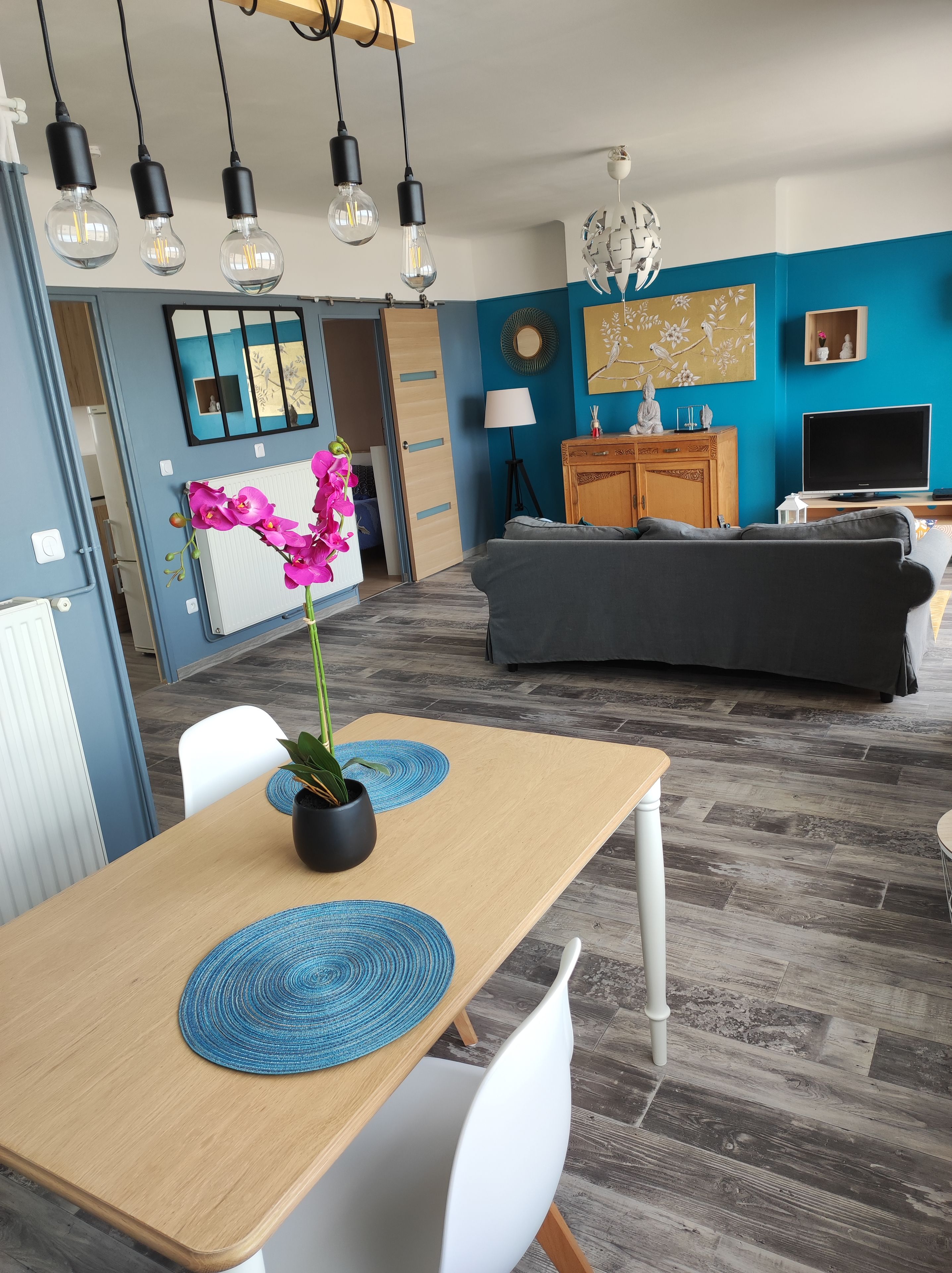 A modern living room with a dining area, a kitchen in the background, and a blue accent wall.