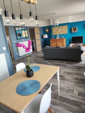 Een moderne woonkamer met een eethoek, een keuken achtergrond en een blauwe accentmuur.