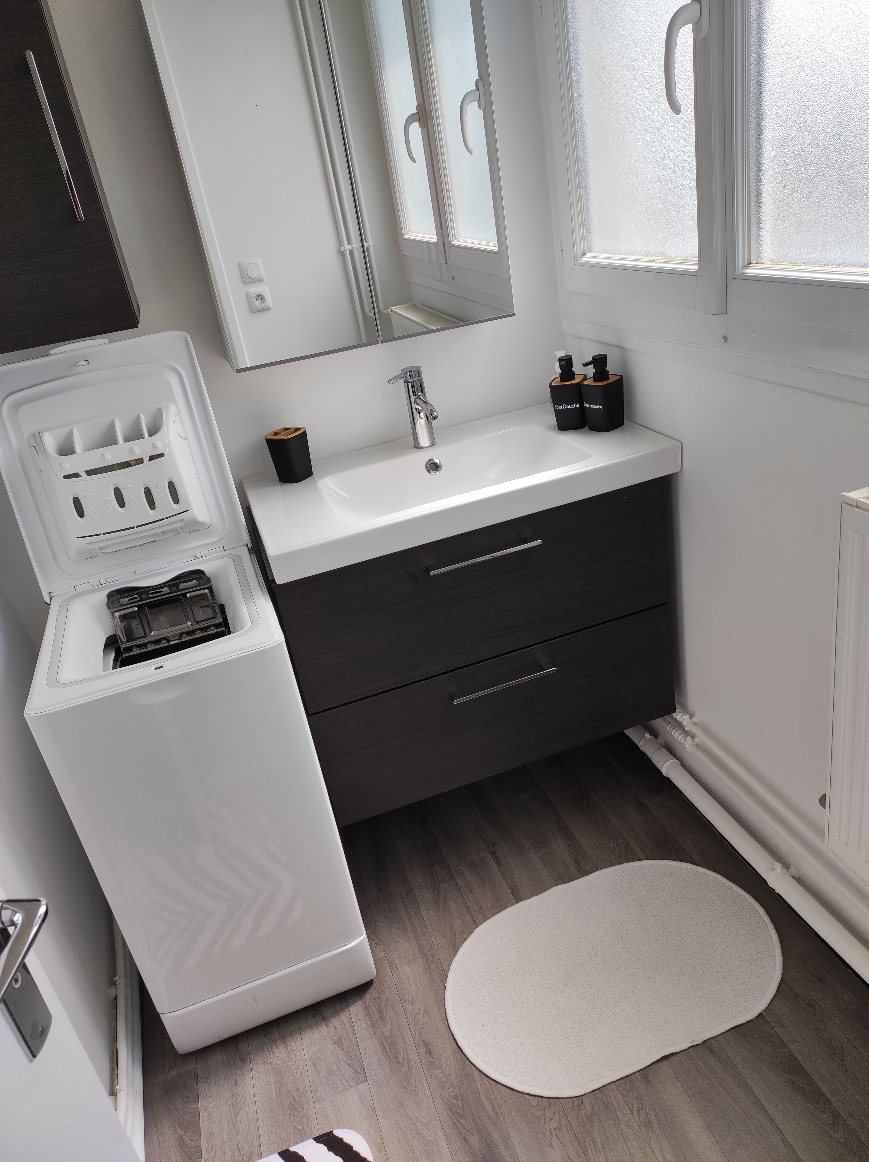 Een moderne badkamer met een witte wastafel, donkere kastjes en een ingebouwd ijsdispenser.