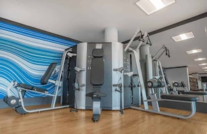 Een sportschool met diverse fitnessapparaten, een bank en een muur met een blauw-wit abstract ontwerp.