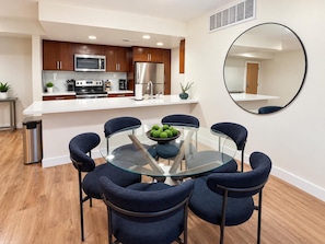 A modern kitchen with a microwave, stove, and refrigerator. There is a dining area with a glass table and chairs. - Blue Marina' Marina And Pool View Top Floor Pool, Gym, Jacuzzi (Marina del Rey)