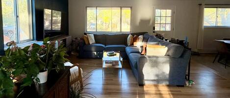 Un salon comprenant un canapé d’angle, une table basse et un téléviseur. De grandes fenêtres laissent entrer la lumière naturelle et offrent une vue sur l’extérieur.