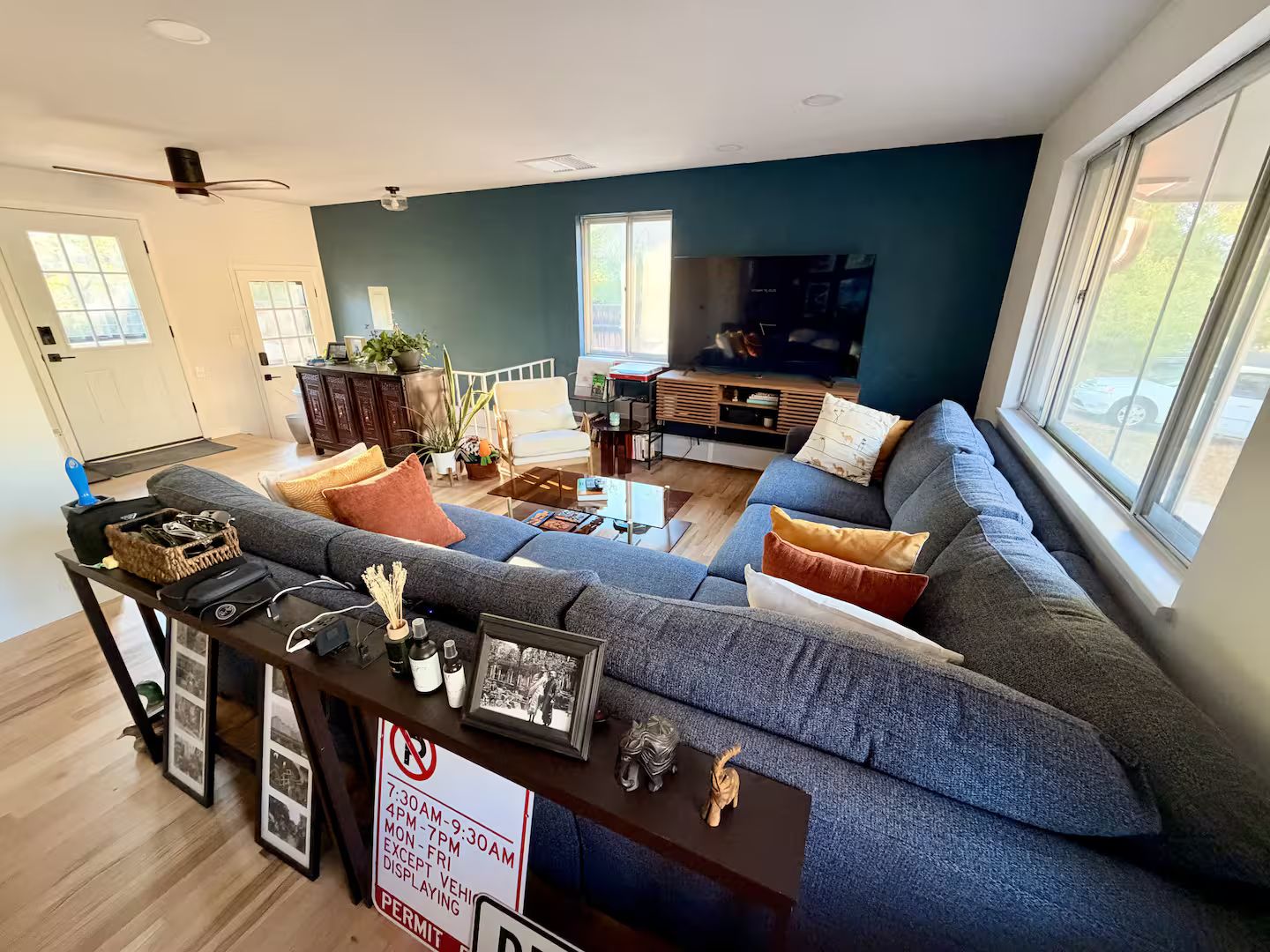 A living room with a large gray sectional sofa, a coffee table, and a TV. There is a sign indicating parking restrictions.