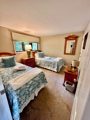 Een hotelkamer met twee bedden, een raam met zonwering, een nachtkastje met lamp, een spiegel en een klein houten kastje.