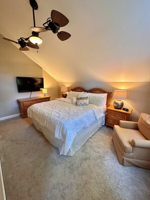 Een slaapkamer met een bed, een plafondventilator, een televisie en een nachtkastje met lamp.