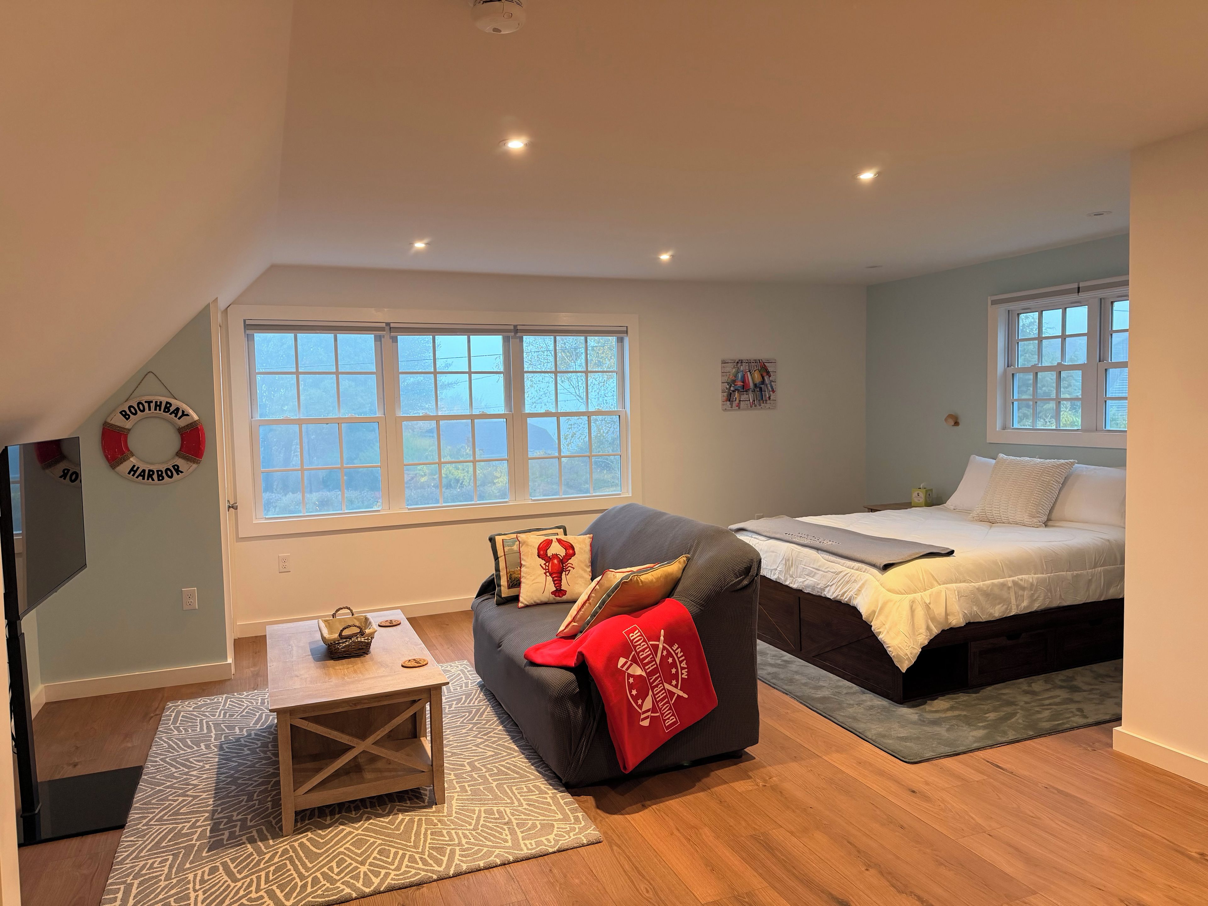 A room with a bed, a sofa, a window, and a wall-mounted life preserver decoration.