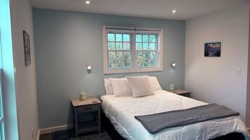 Un dormitorio con cama, mesitas de noche, una ventana y un cuadro en la pared.