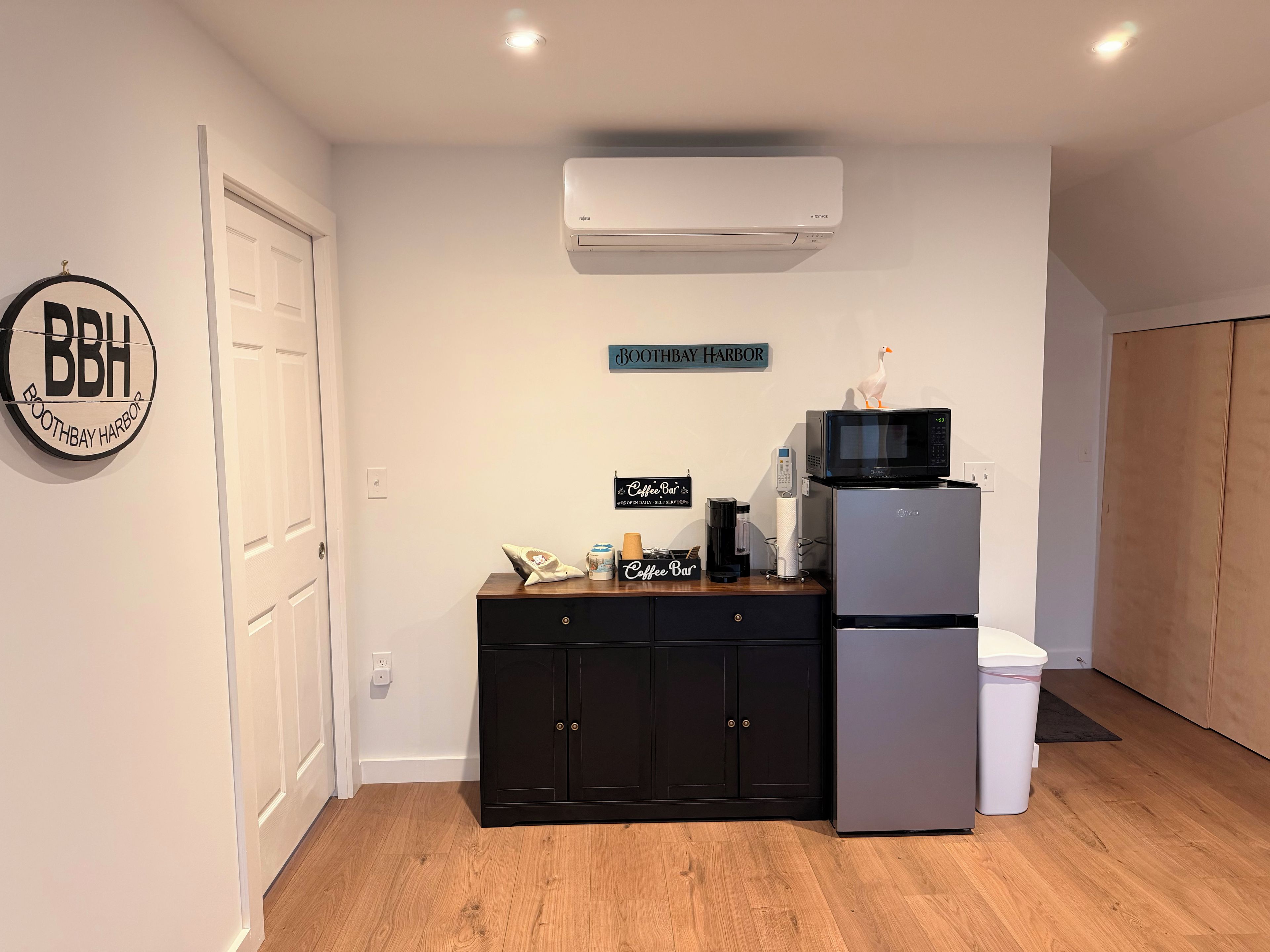Una kitchenette con microondas, refrigerador y cafetera sobre una encimera de madera.