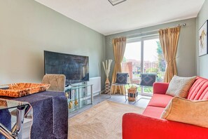 A living room with a red sofa, a glass coffee table, a flat-screen TV, and a view of the outdoors through large windows. - Modern 1BR Flat Near Bullring & Grand Central (Birmingham)