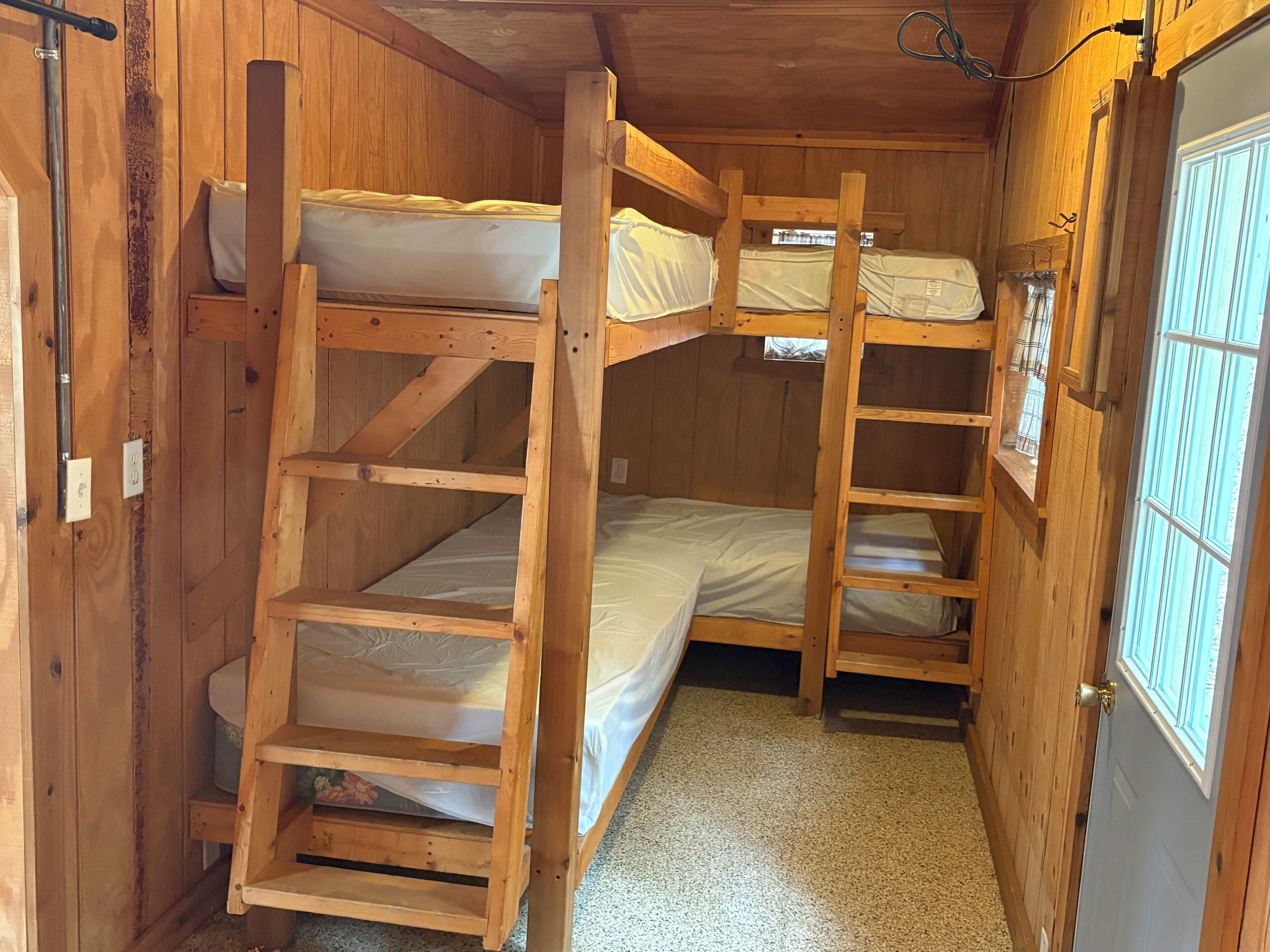 A compact wooden room with bunk beds, a window, and a door.