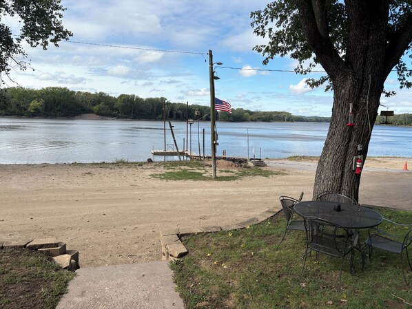 Un espace de pique-nique au bord de la rivière, équipé d’une table et de chaises, d’un drapeau et d’un quai.