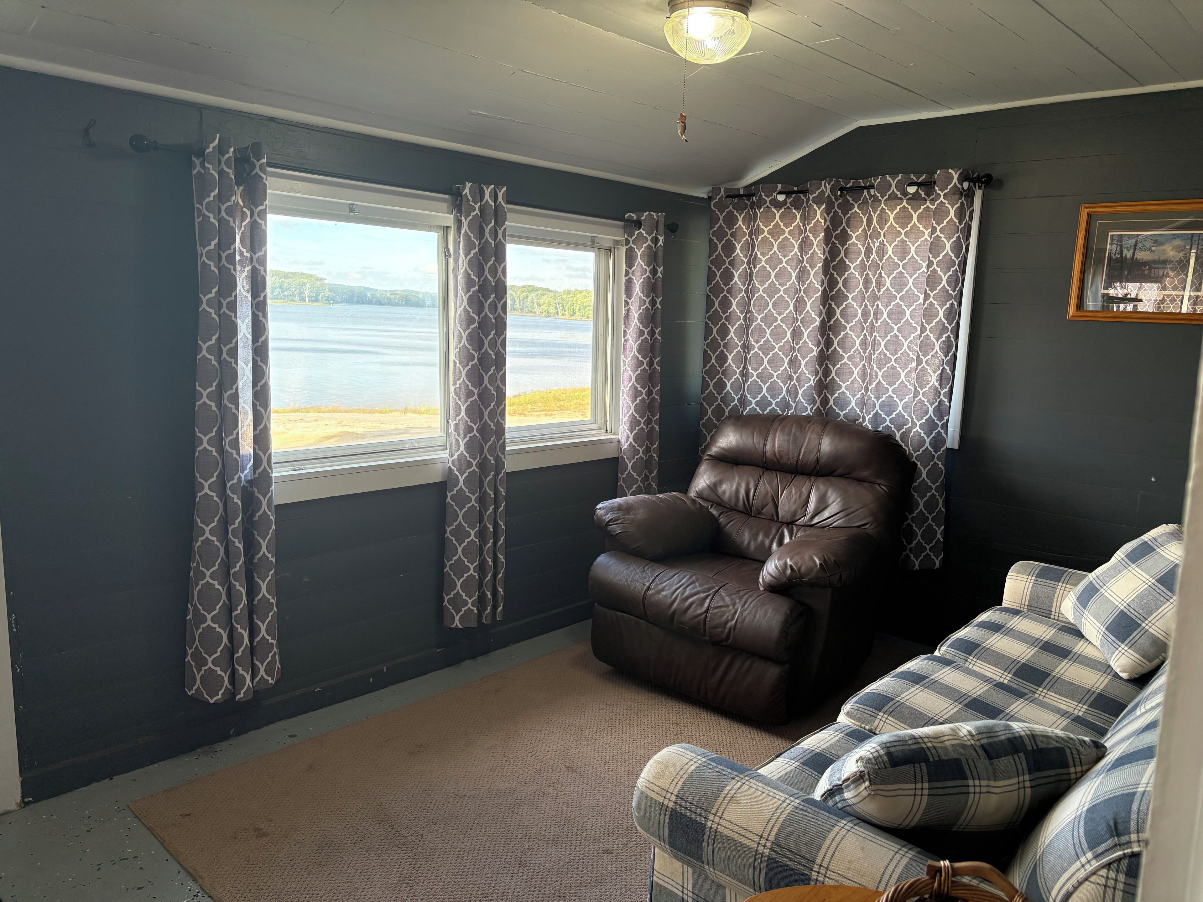 A room with a leather chair, a plaid sofa, and two windows with patterned curtains.