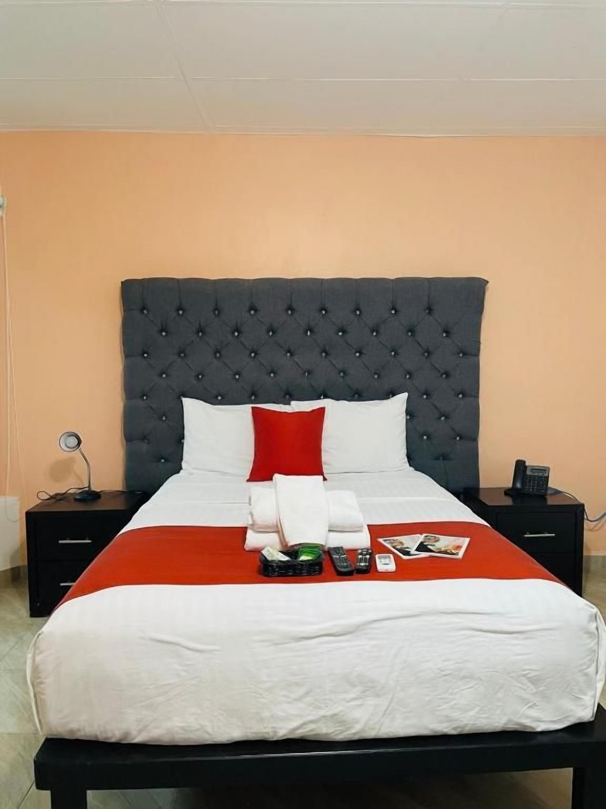 Una cama bien hecha con una colcha roja y blanca, un cabecero capitonado negro y un almohadón blanco.