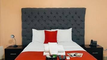 Una cama bien hecha con una colcha roja y blanca, un cabecero capitonado negro y un almohadón blanco.