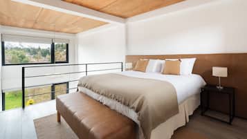 Un dormitorio moderno con una cama grande, un banco, una mesita de noche y vistas al exterior.