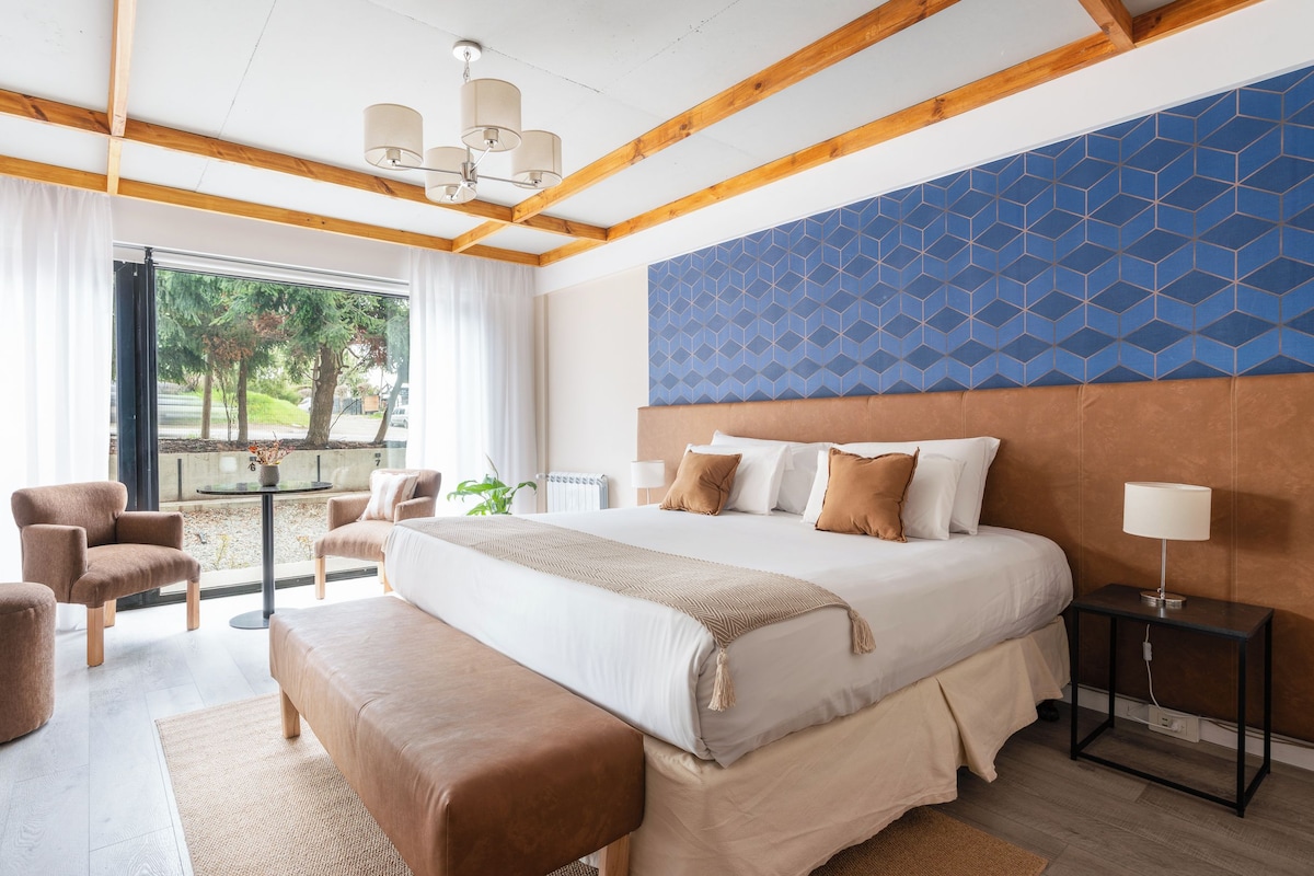 A hotel room with a large bed, a seating area with chairs, a small table, and a view of the outdoors.