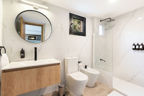 A modern bathroom with a marble backsplash, a round mirror, a toilet, a bidet, and a shower area. - Villa Sofia Suites (San Carlos de Bariloche)