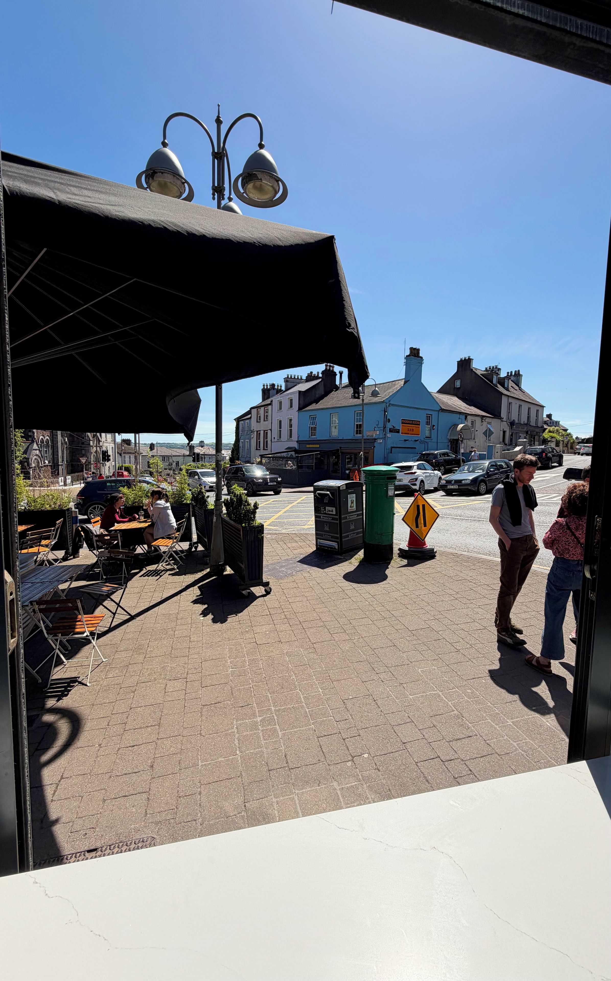 A street view with outdoor seating, a blue building with signage, and a pedestrian crossing.