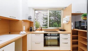 Eine kompakte Küche mit Backofen, Kaffeemaschine und Fenster mit Blick auf ein Wohngebäude.