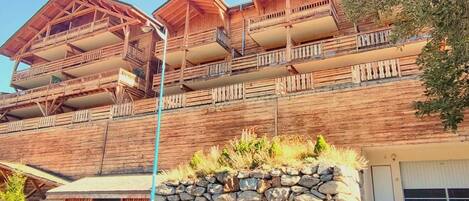 A multi-story wooden building with balconies, a stone wall in front, and a garage.