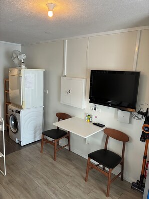 A compact room with a washing machine, a table with two chairs, a mounted TV, and a ceiling light. - Cozy studioapartment with free parking (Reykjavík)
