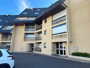 Un immeuble résidentiel à plusieurs étages, doté de balcons, d’un espace de stationnement et d’une entrée sécurisée par un portail.