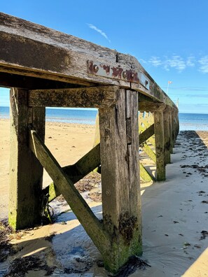 Une jetée en bois, agrémentée d’un panneau indicateur, qui mène à une plage de sable.