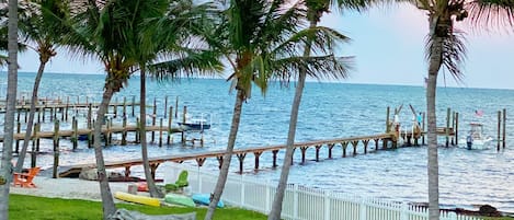 A pier extending into calm waters with palm trees and a white fence along its length.