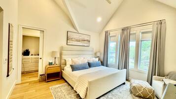 A bedroom with a bed, bedside tables, a ceiling fan, a window with curtains, and a view of greenery outside.