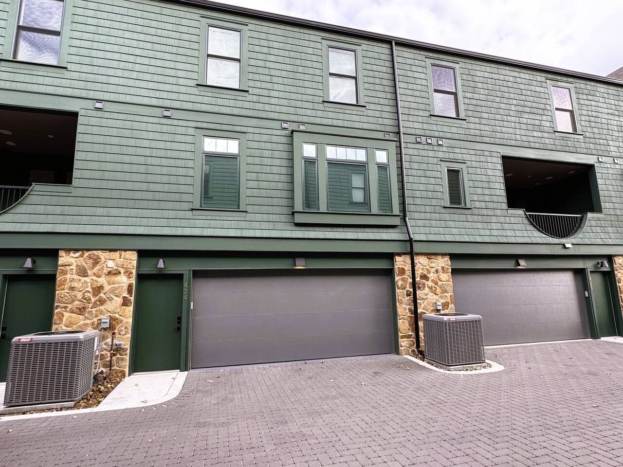 En toetages bygning med grøn facade, to garagedøre og en murstensvæg.