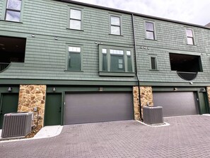 En toetages bygning med grøn facade, to garagedøre og en murstensvæg.