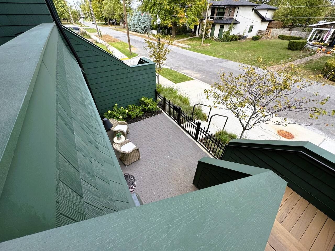 En boligejendom med facade i grøn farve, en anlagt terrasse med udendørs møbler og udsigt til gaden og omkringliggende huse.