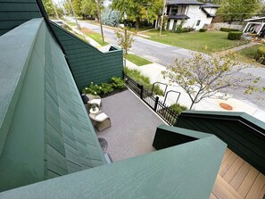 En boligejendom med facade i grøn farve, en anlagt terrasse med udendørs møbler og udsigt til gaden og omkringliggende huse.