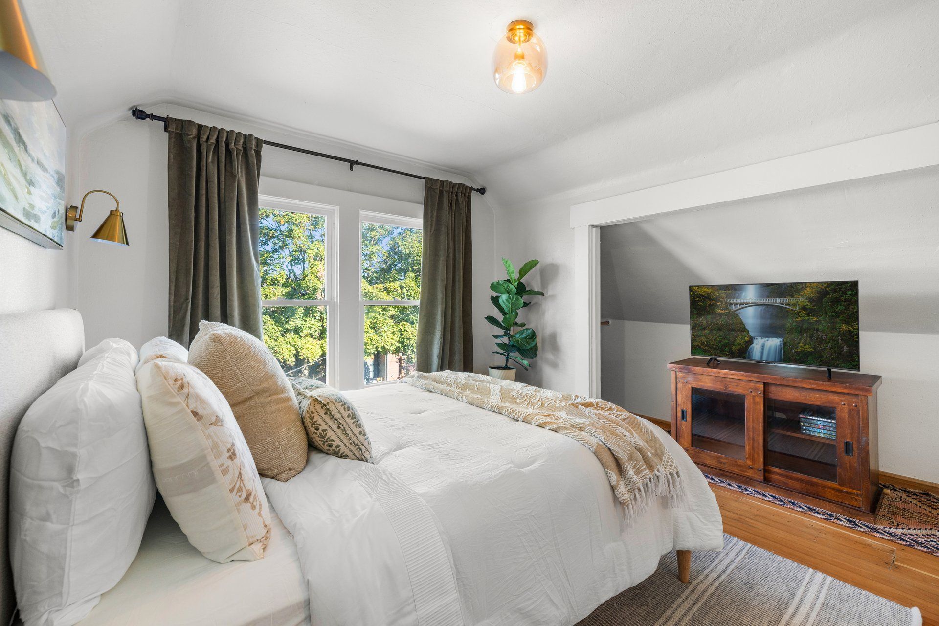 Un dormitorio con una cama grande, un televisor sobre un mueble de madera y una ventana con cortinas.