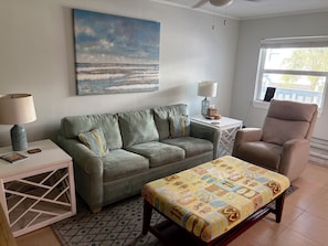 A living room with a sofa, armchair, coffee table, and a painting of a beach scene. - Boca Ciega Bay Hideaway - Rest, Relax, Renew (Treasure Island)