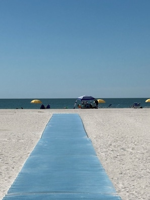 A beach with a blue mat leading to a shaded area with umbrellas. - Boca Ciega Bay Hideaway - Rest, Relax, Renew (Treasure Island)