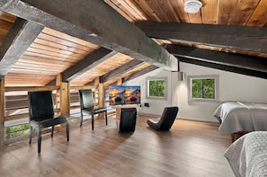 A spacious attic room with wooden beams, a large TV screen, and a bed.