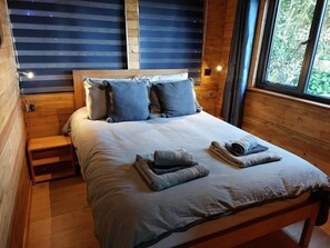 A bed with a wooden headboard, pillows, and a blanket. - Cabin Sleeps 2 With Wifi and Heating (St Austell)