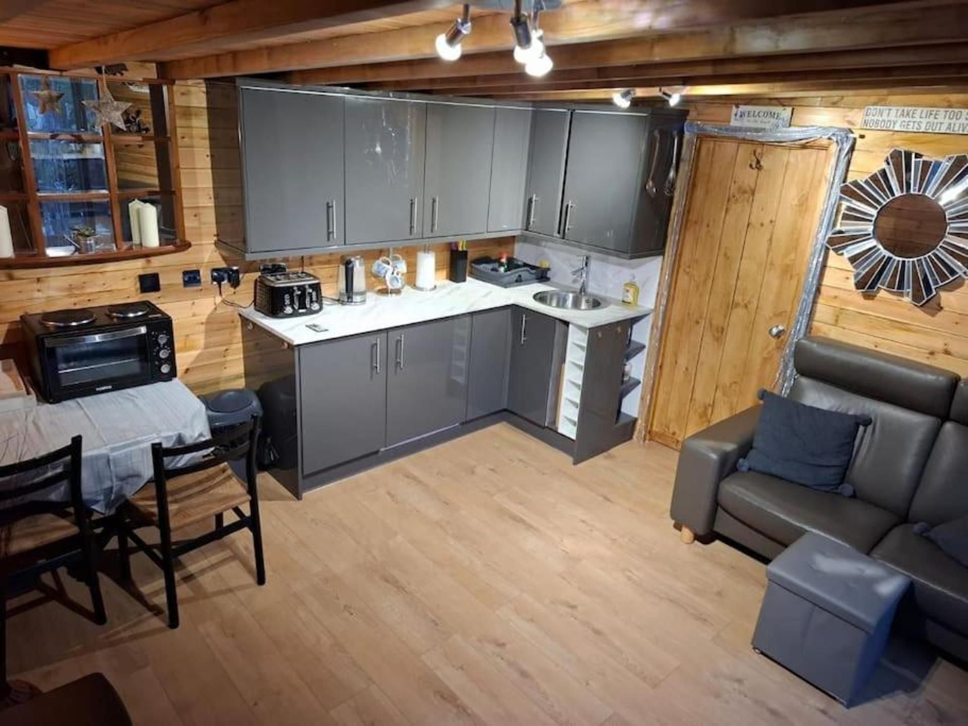 A compact kitchen with grey cabinets, a built-in oven, and a sink. There's a dining area with a table and chairs, and a sofa.