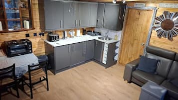 A compact kitchen with grey cabinets, a built-in oven, and a sink. There's a dining area with a table and chairs, and a sofa.