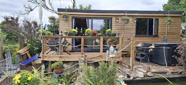 A wooden deck with a hot tub, surrounded by potted plants and a small garden. - Cabin Sleeps 2 With Wifi and Heating (St Austell)