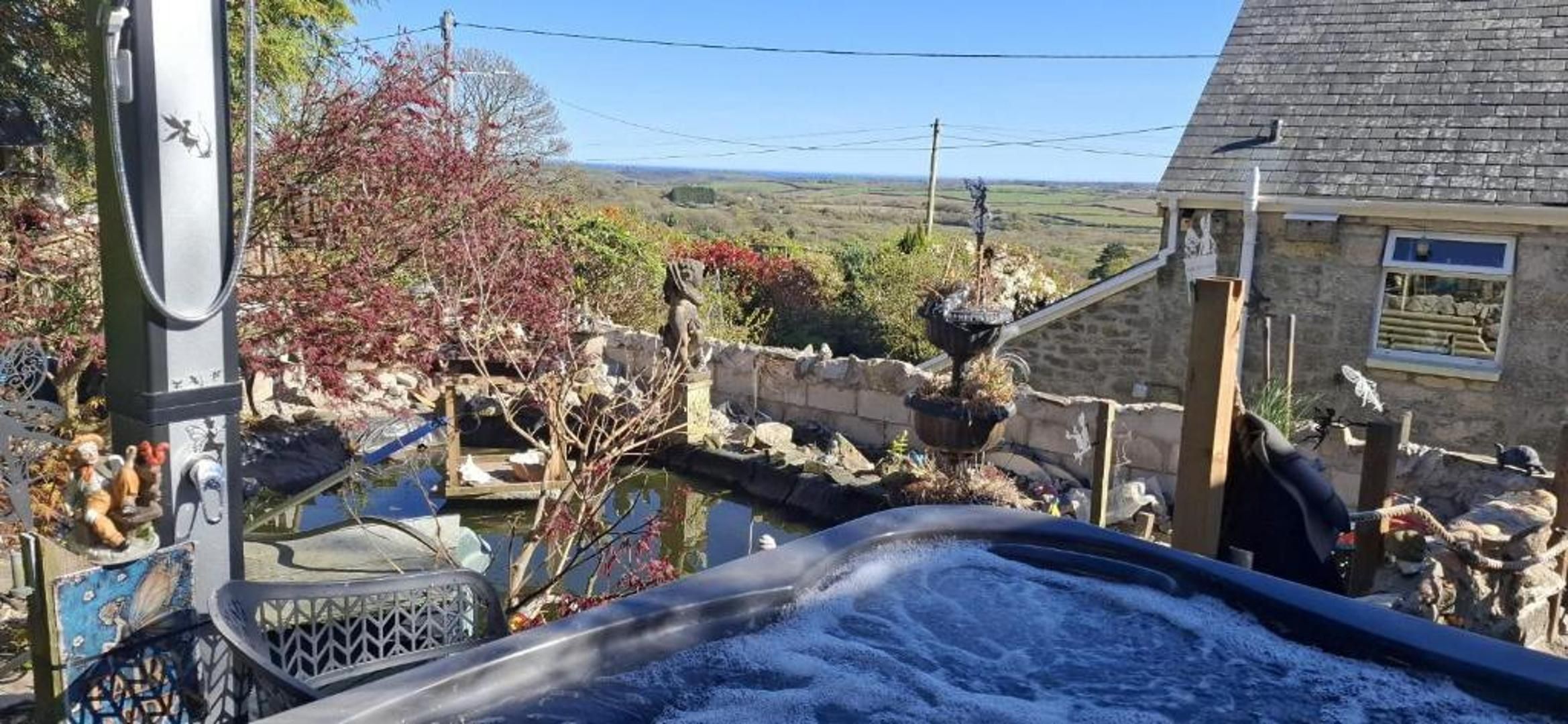 Un espacio al aire libre rústico con un jacuzzi, construcciones de piedra y vistas al campo.