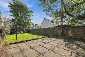A paved courtyard with a grassy area, a stone wall, and residential buildings in the background. - Underfloor Heating | Luxury Aberdeen City Centre Apartment 2 Bedrooms (Aberdeen)