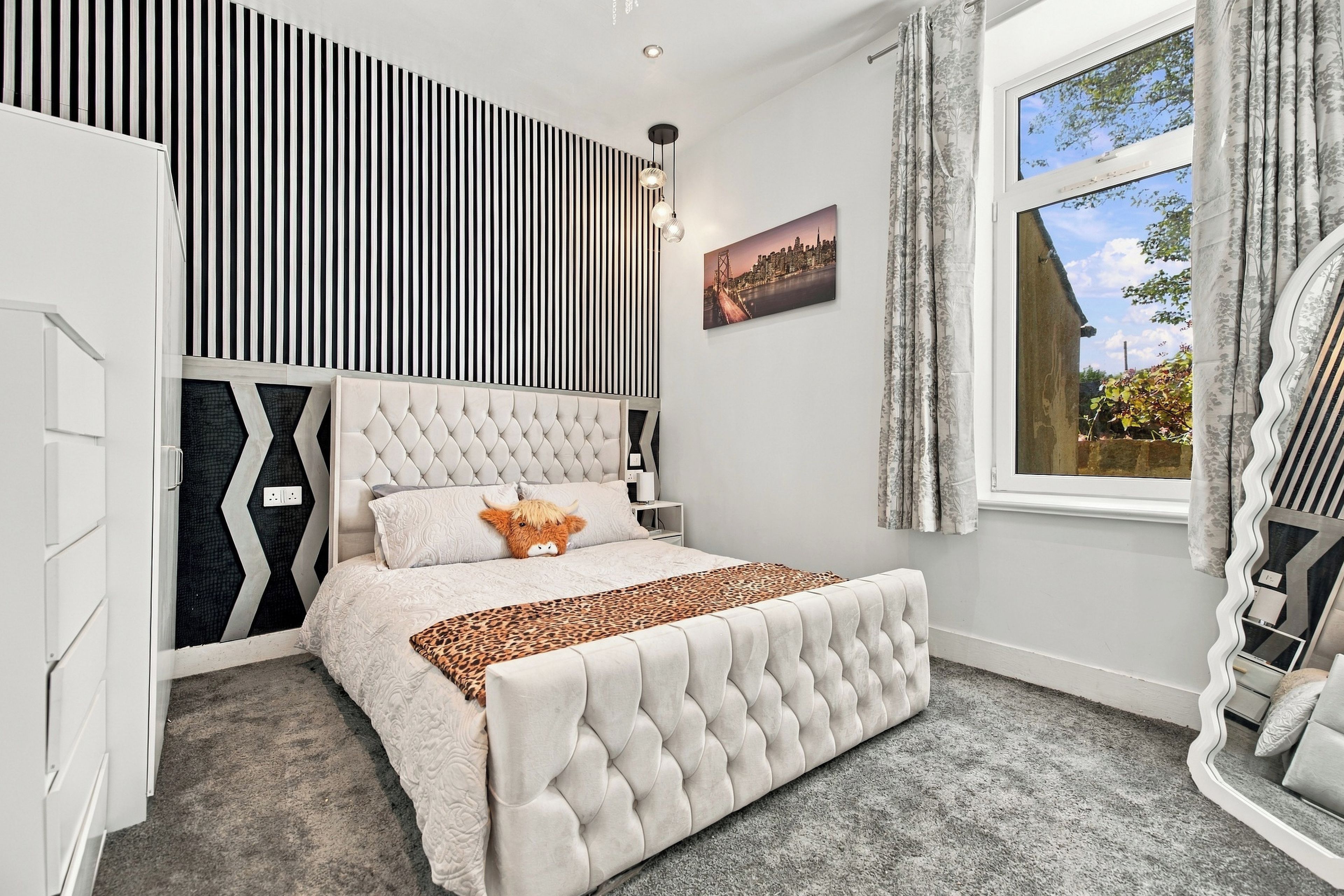 A bedroom with a large bed, a cityscape painting, and a window with curtains.
